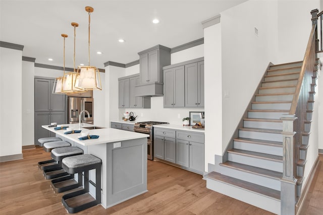 kitchen featuring appliances with stainless steel finishes, sink, light hardwood / wood-style floors, decorative light fixtures, and a center island with sink