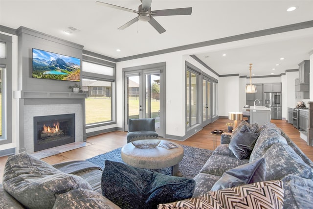 living room with crown molding, light wood-type flooring, a fireplace, and ceiling fan