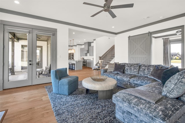 living room with crown molding, a barn door, light wood-type flooring, and ceiling fan