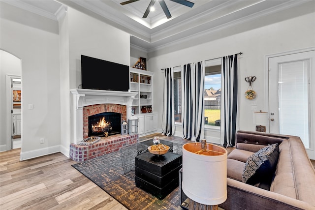 living room featuring ceiling fan, light hardwood / wood-style flooring, a fireplace, a towering ceiling, and crown molding