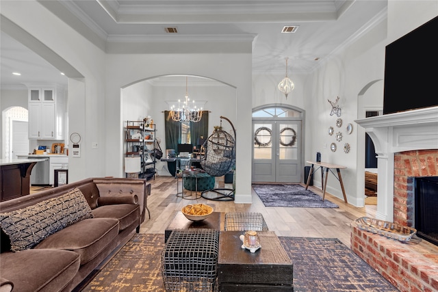 living room featuring a brick fireplace, light hardwood / wood-style flooring, ornamental molding, a towering ceiling, and a notable chandelier