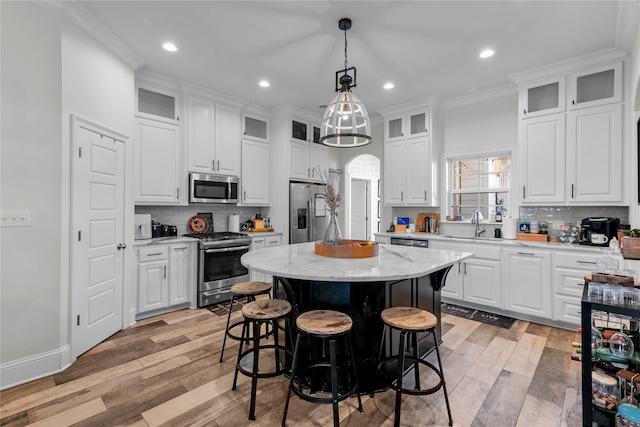 kitchen featuring light wood-type flooring, a center island, white cabinetry, stainless steel appliances, and ornamental molding