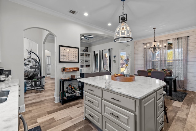 kitchen featuring ornamental molding, a center island, light stone counters, and light wood-type flooring