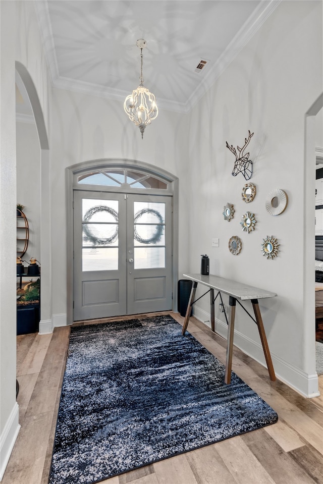 entrance foyer featuring french doors, crown molding, a chandelier, and light wood-type flooring