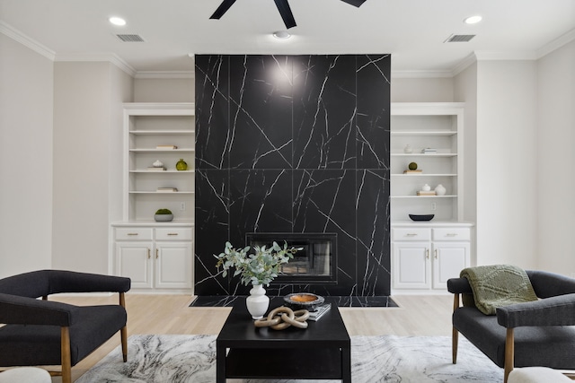 living room featuring a high end fireplace, ceiling fan, crown molding, light hardwood / wood-style flooring, and built in shelves