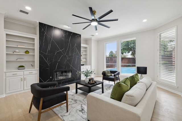 living room featuring a premium fireplace, crown molding, light hardwood / wood-style floors, and ceiling fan