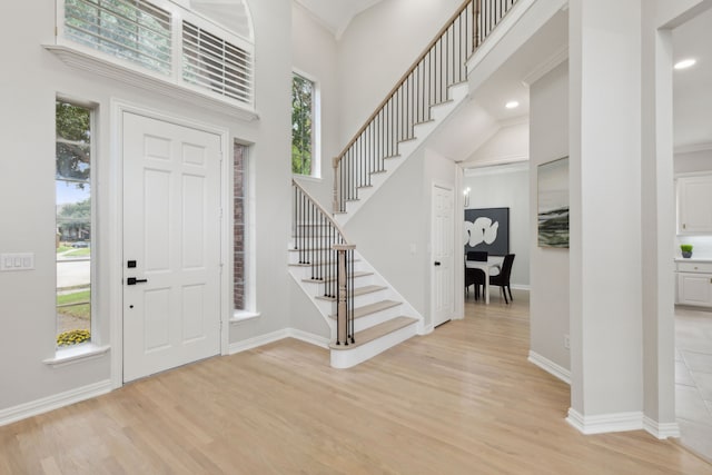 foyer featuring crown molding, a high ceiling, and light wood-type flooring