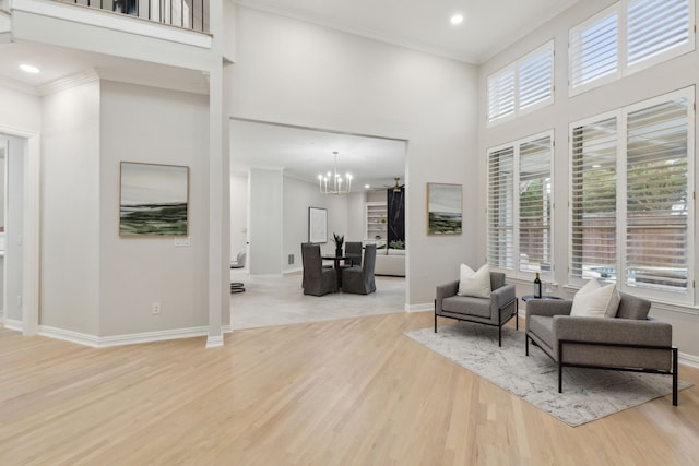 living room with light hardwood / wood-style floors, an inviting chandelier, ornamental molding, and a high ceiling