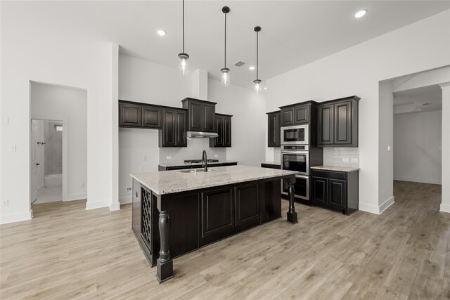 kitchen featuring built in microwave, a high ceiling, light stone counters, an island with sink, and pendant lighting