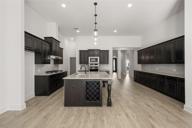 kitchen featuring tasteful backsplash, appliances with stainless steel finishes, a center island with sink, and hanging light fixtures