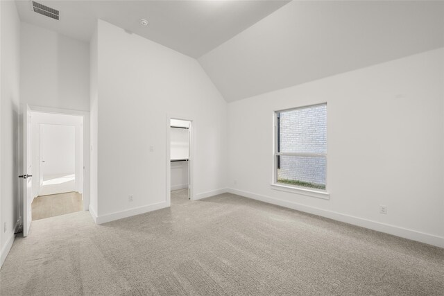 unfurnished bedroom featuring light carpet, a spacious closet, a closet, and lofted ceiling