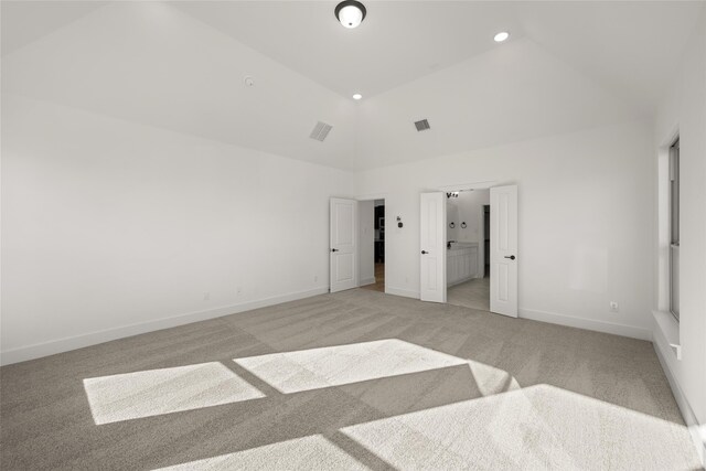 unfurnished bedroom featuring light carpet, ensuite bathroom, and high vaulted ceiling