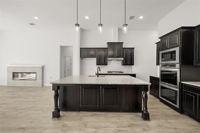 kitchen featuring sink, hanging light fixtures, light stone counters, a kitchen island with sink, and appliances with stainless steel finishes