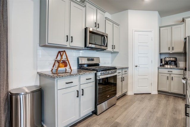 kitchen featuring stainless steel appliances, dark stone countertops, light hardwood / wood-style flooring, and backsplash