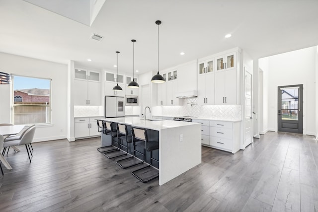 kitchen featuring stainless steel microwave, an island with sink, a kitchen breakfast bar, white cabinetry, and dark hardwood / wood-style floors