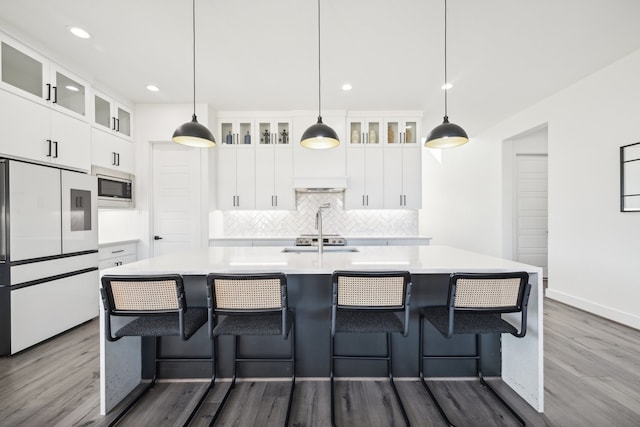 kitchen with hardwood / wood-style flooring, stainless steel microwave, high end white fridge, a center island with sink, and decorative light fixtures