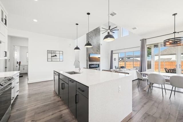 kitchen featuring stainless steel range with electric cooktop, dark hardwood / wood-style flooring, a kitchen island with sink, sink, and decorative light fixtures