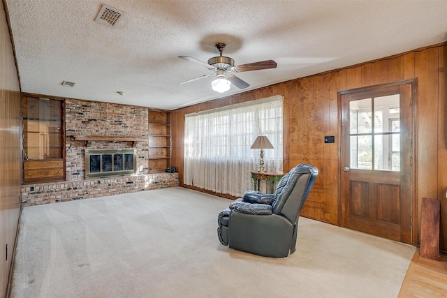 living area with wood walls, a fireplace, a textured ceiling, built in features, and ceiling fan