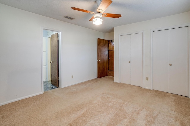 unfurnished bedroom with light carpet, a textured ceiling, multiple closets, and ceiling fan