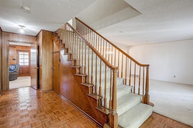 staircase with parquet flooring, wood walls, and a textured ceiling