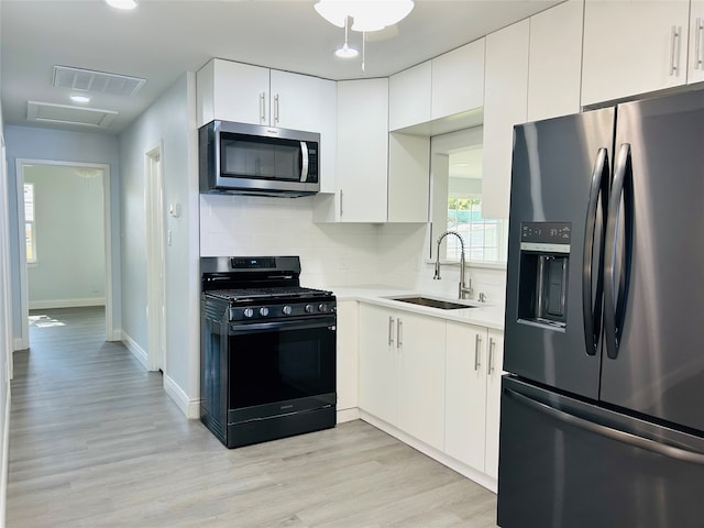 kitchen with backsplash, sink, white cabinetry, appliances with stainless steel finishes, and light hardwood / wood-style floors