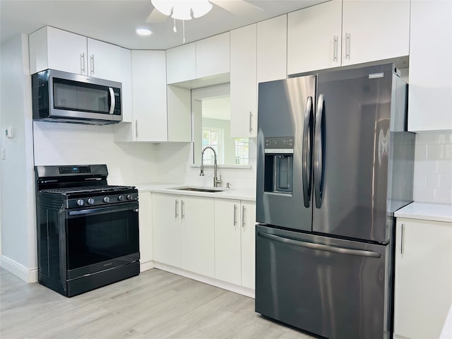 kitchen featuring sink, light wood-type flooring, stainless steel appliances, white cabinets, and decorative backsplash