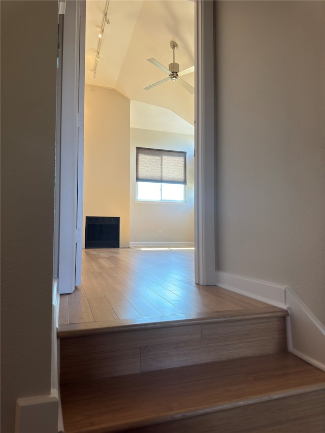 corridor featuring hardwood / wood-style flooring, rail lighting, and vaulted ceiling