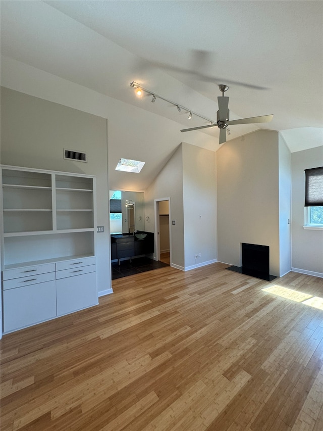 unfurnished living room featuring lofted ceiling with skylight, rail lighting, light hardwood / wood-style floors, and ceiling fan