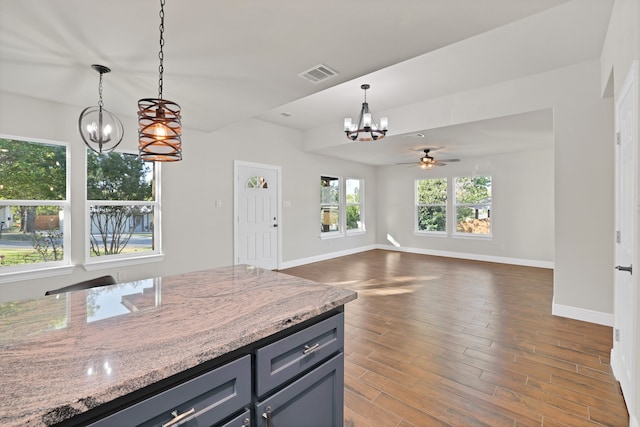 kitchen with light stone countertops, dark wood-type flooring, ceiling fan with notable chandelier, and pendant lighting