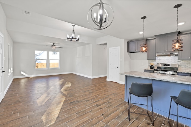 kitchen with gray cabinets, stainless steel range with gas cooktop, a breakfast bar, and dark hardwood / wood-style flooring