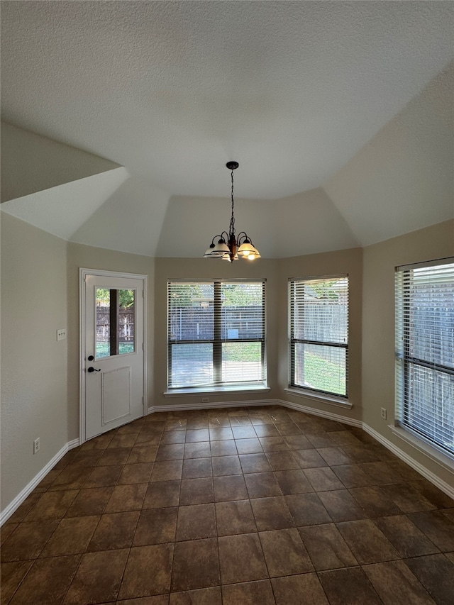 unfurnished dining area featuring an inviting chandelier, dark tile patterned flooring, a textured ceiling, and vaulted ceiling