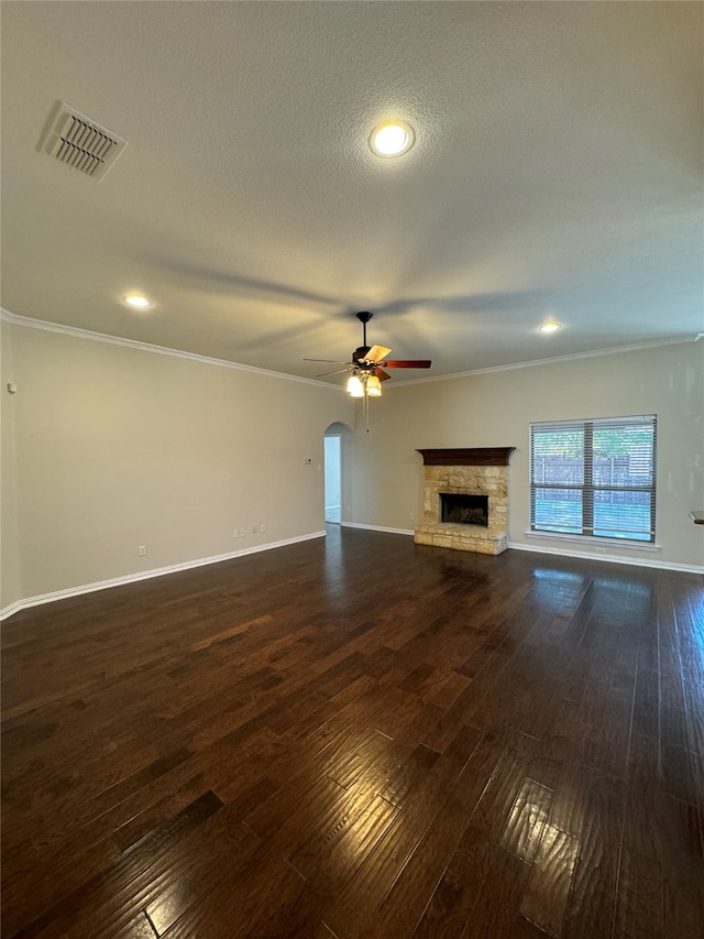 unfurnished living room with crown molding, ceiling fan, a stone fireplace, and dark hardwood / wood-style flooring