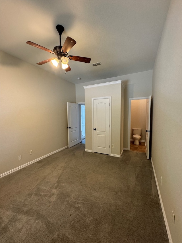 unfurnished bedroom featuring ensuite bath, dark carpet, and ceiling fan