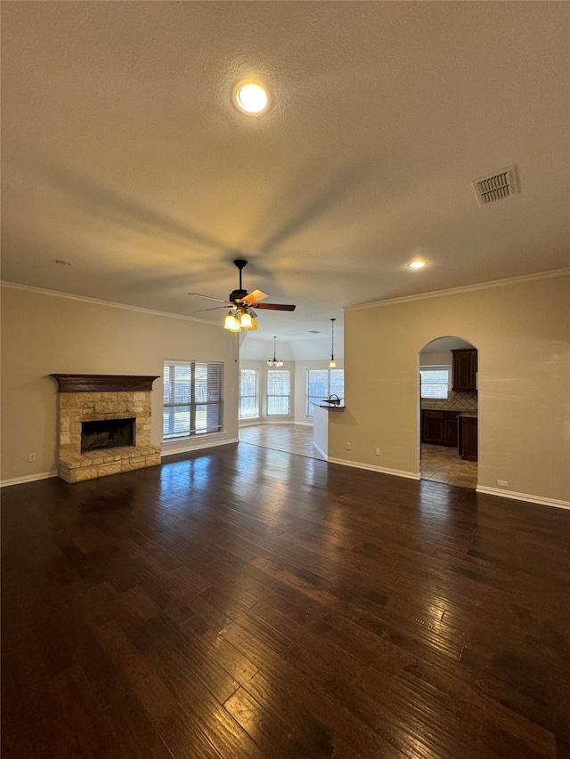 unfurnished living room with a stone fireplace, ornamental molding, ceiling fan, and dark hardwood / wood-style flooring