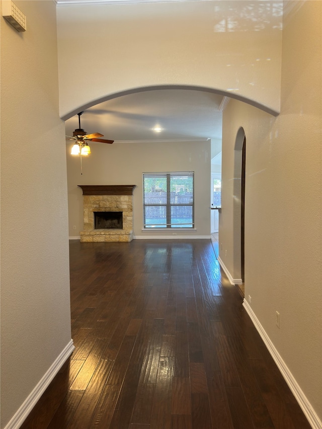 unfurnished living room featuring ornamental molding, dark wood-type flooring, a stone fireplace, and ceiling fan