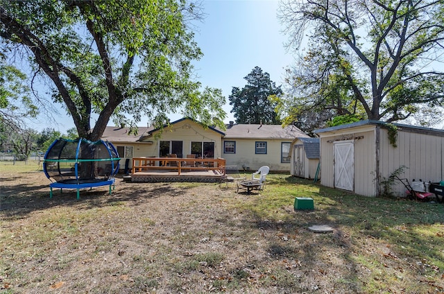 rear view of property with a shed, a yard, an outdoor fire pit, a trampoline, and a deck