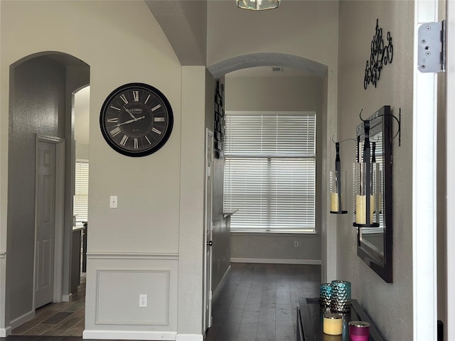 corridor featuring baseboards, arched walkways, and dark wood-style flooring