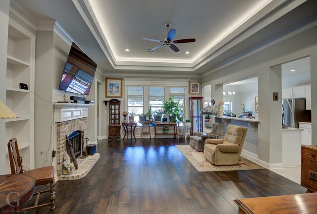 living area with ornamental molding, dark hardwood / wood-style flooring, a brick fireplace, and ceiling fan with notable chandelier