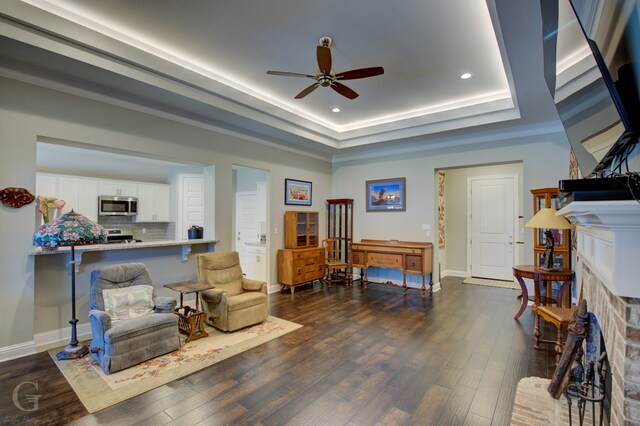 living area with ornamental molding, ceiling fan, a raised ceiling, and dark hardwood / wood-style flooring