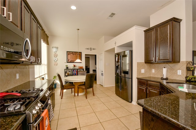 kitchen with stainless steel appliances, dark brown cabinetry, dark stone counters, pendant lighting, and decorative backsplash