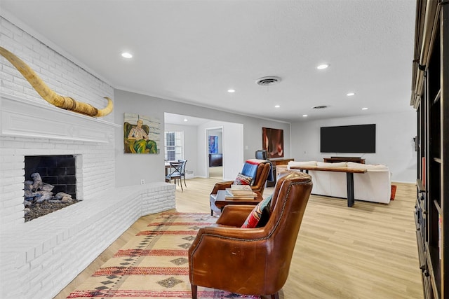 living room featuring a textured ceiling, a fireplace, light hardwood / wood-style floors, and brick wall