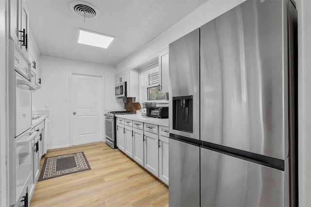 kitchen featuring white cabinets, a textured ceiling, appliances with stainless steel finishes, and light hardwood / wood-style flooring