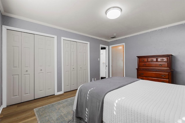 bedroom with hardwood / wood-style floors, ornamental molding, and multiple closets