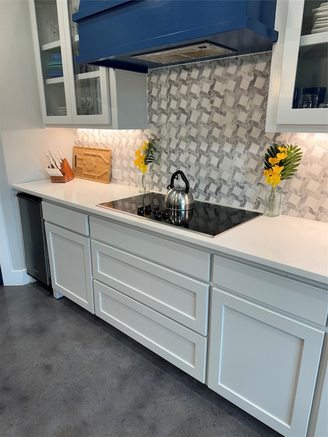 kitchen with black electric stovetop, custom range hood, stainless steel dishwasher, white cabinets, and tasteful backsplash