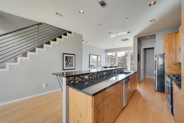 kitchen featuring a spacious island, dark stone counters, sink, light wood-type flooring, and appliances with stainless steel finishes