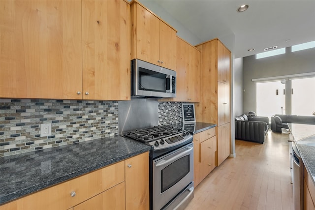 kitchen with appliances with stainless steel finishes, light hardwood / wood-style flooring, dark stone countertops, and decorative backsplash