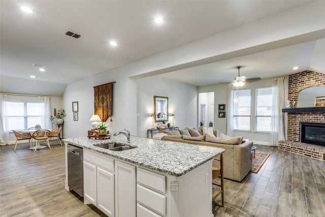 kitchen featuring lofted ceiling, a center island with sink, sink, light wood-type flooring, and white cabinetry