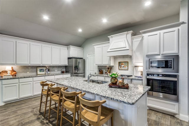 kitchen with a breakfast bar area, a center island with sink, sink, appliances with stainless steel finishes, and dark hardwood / wood-style flooring