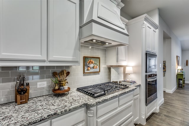 kitchen featuring decorative backsplash, premium range hood, white cabinetry, light wood-type flooring, and stainless steel appliances