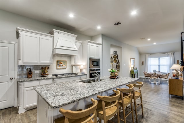 kitchen with a breakfast bar area, custom exhaust hood, an island with sink, and stainless steel appliances